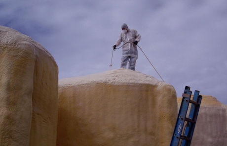 Man on roof spray foaming water tanks in central New Mexico